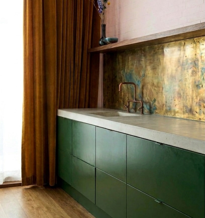 Modern kitchen with green cabinets, concrete countertop, and aged brass backsplash with verdigris accents

