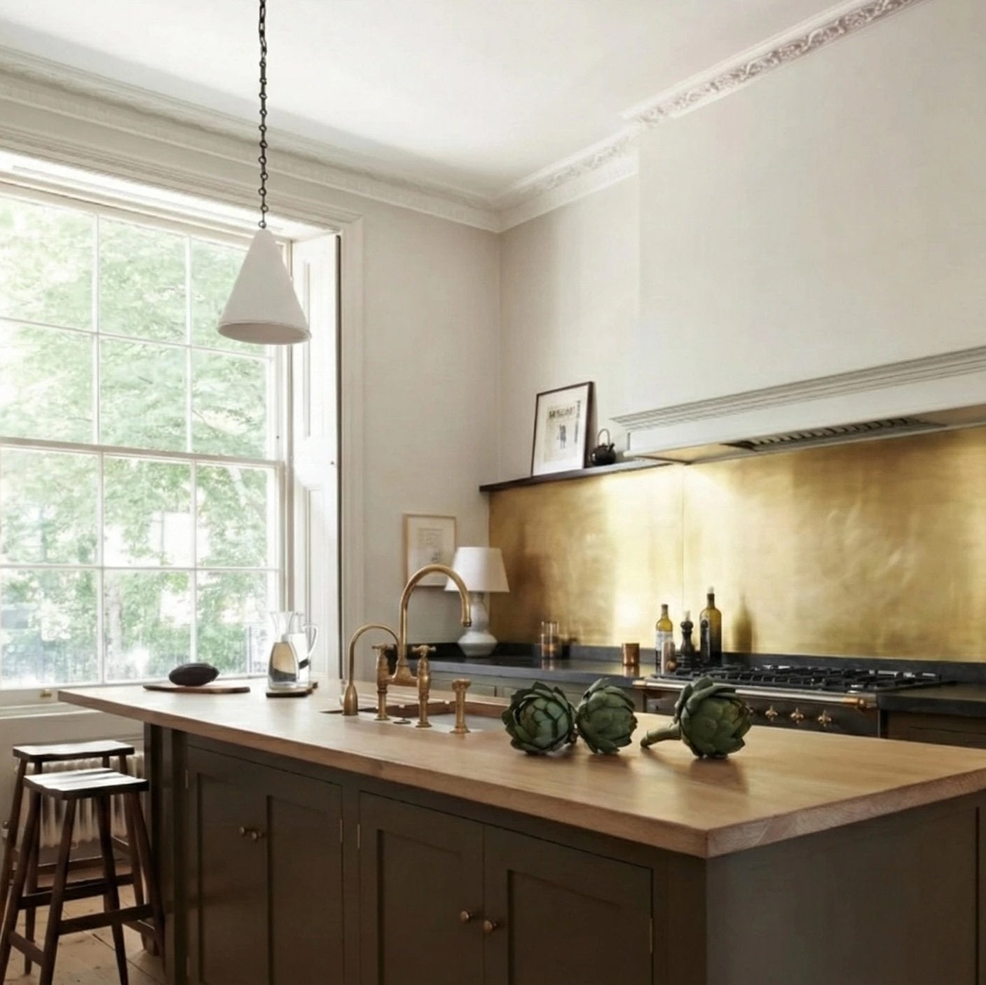 Bespoke brass backsplash in olive-green georgian style kitchen, with wooden worktops and floating shelves. 
