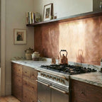 Bespoke copper splashback in a Georgian kitchen with dark wood cabinets and floating oak shelve. Copper backsplash is installed above marble worktop, above gas hob. 