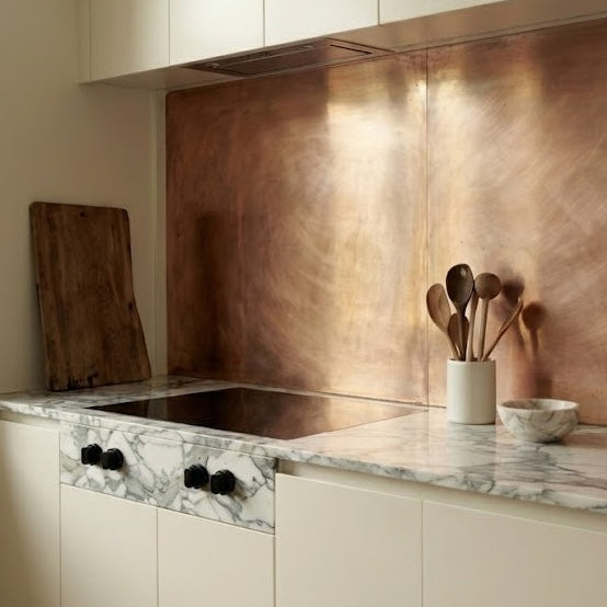 Brushed copper splashback, installed in a modern off-white kitchen with gray&white marble countertop