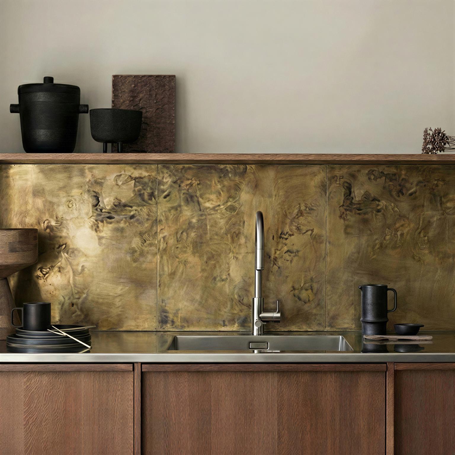 Aged brass kitchen splashback installed below an integrated wooden shelf, paired with a stainless steel worktop in a Japandi kitchen with oak cabinets
