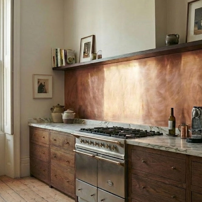 Brushed copper splashback in a classic kitchen with dark wood cabinets, marble countertops, gas hob and floating shelf.