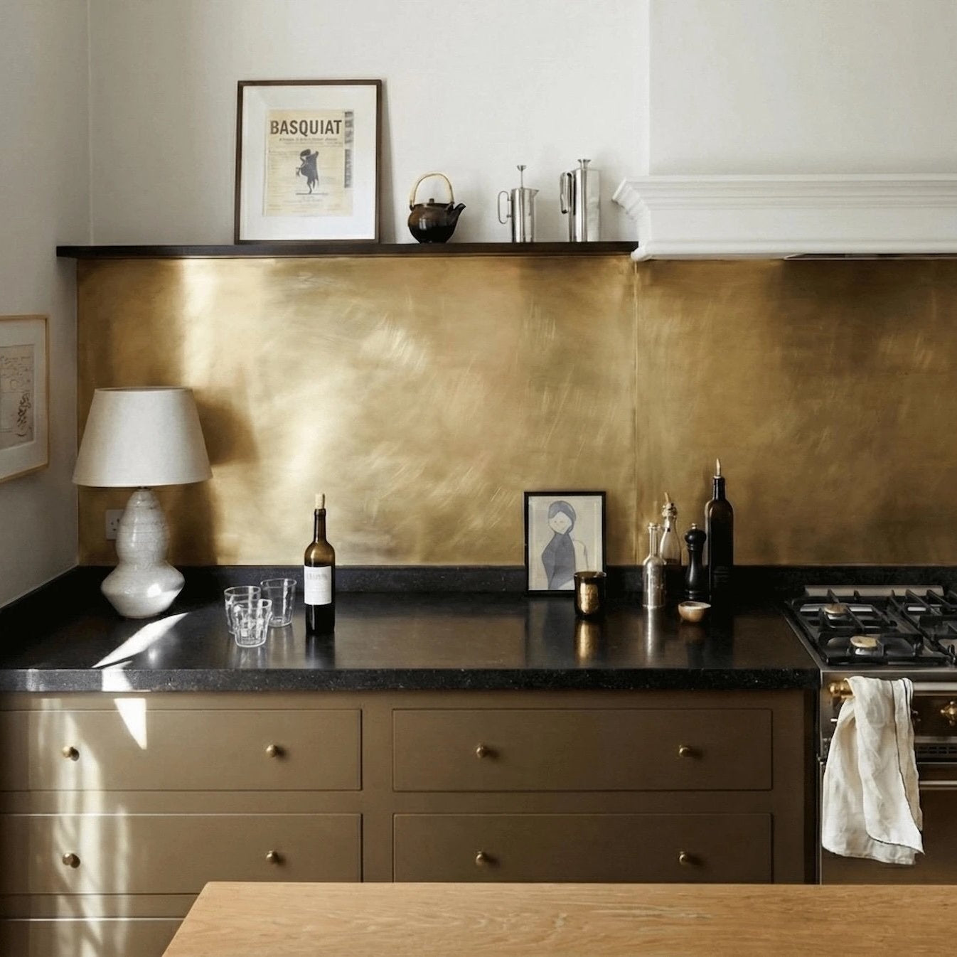 Luxury kitchen interior with a brushed brass backsplash, olive green cabinetry, and integrated gold-toned wall paneling for a warm, metallic finish