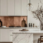 Bespoke brushed copper splashback installed in a luxury white kitchen, featuring a mouldings, marble waterfall island and minimalist white cabinetry.