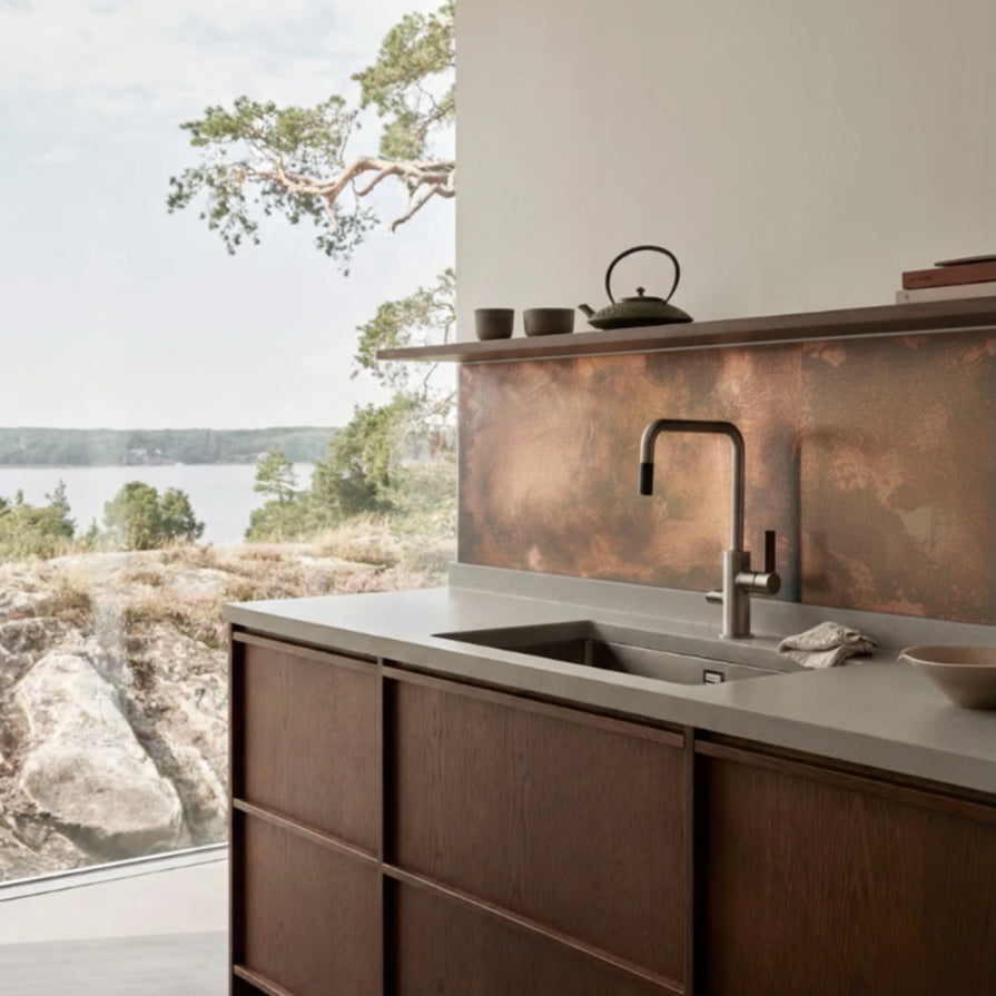 Modern Japandi kitchen with copper backsplash and sink, overlooking a scenic view.

