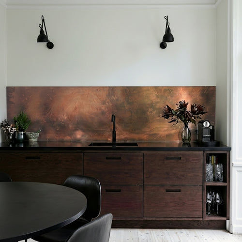 Modern kitchen with wooden cabinets, a copper backsplash, and black fixtures. Copper patina features black, orange and dark-green hues.