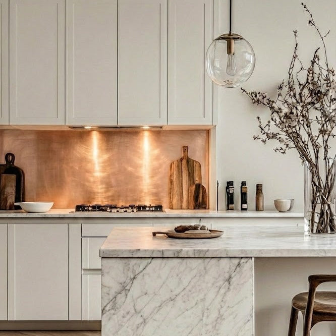 Modern kitchen with marble island, copper backsplash, and white cabinets.

